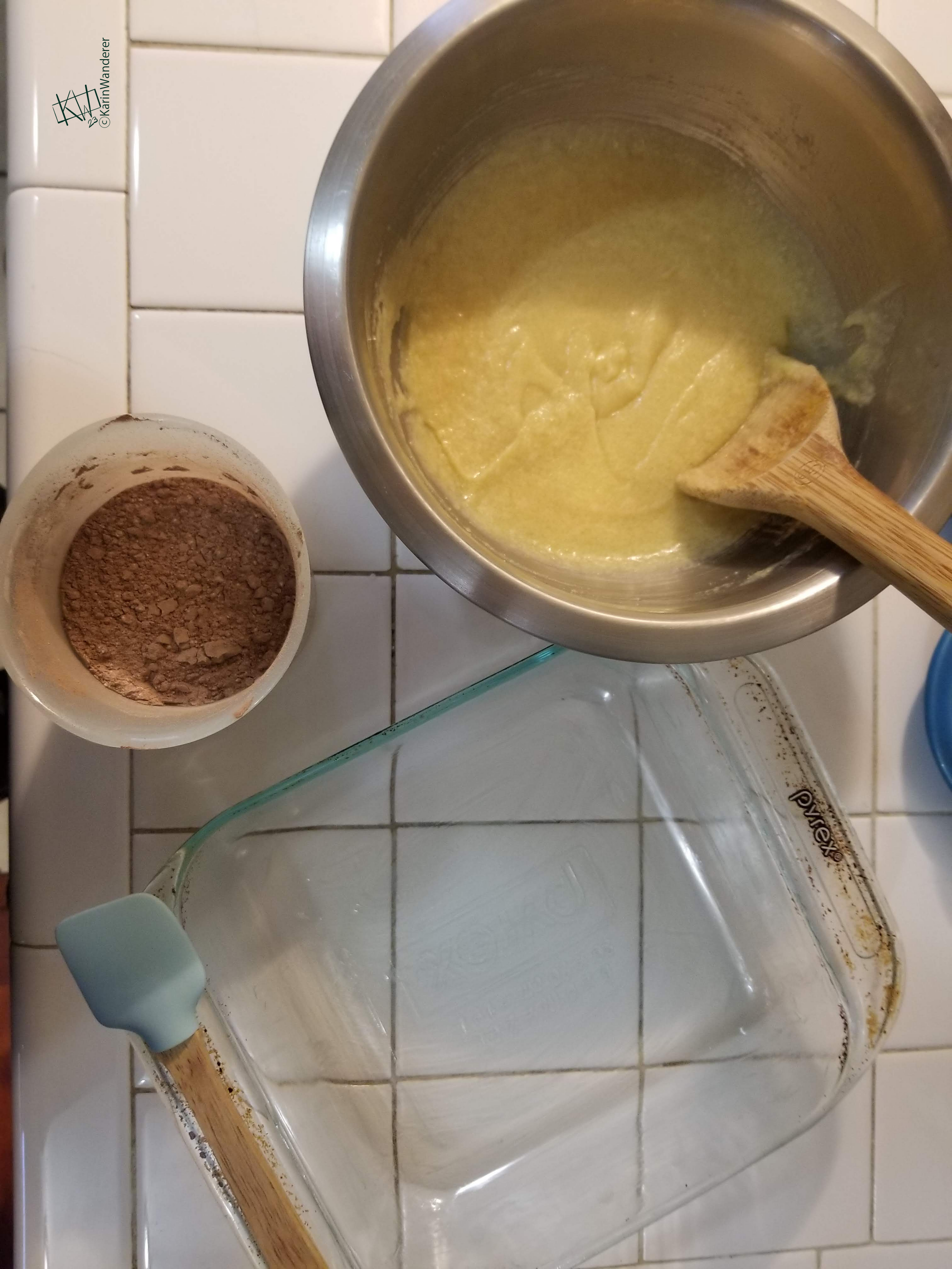Photo of a bowl with the wet ingredients for brownies & a cup with the dry ingredients. A square glass baking dish & rubber spatula wait next to them.