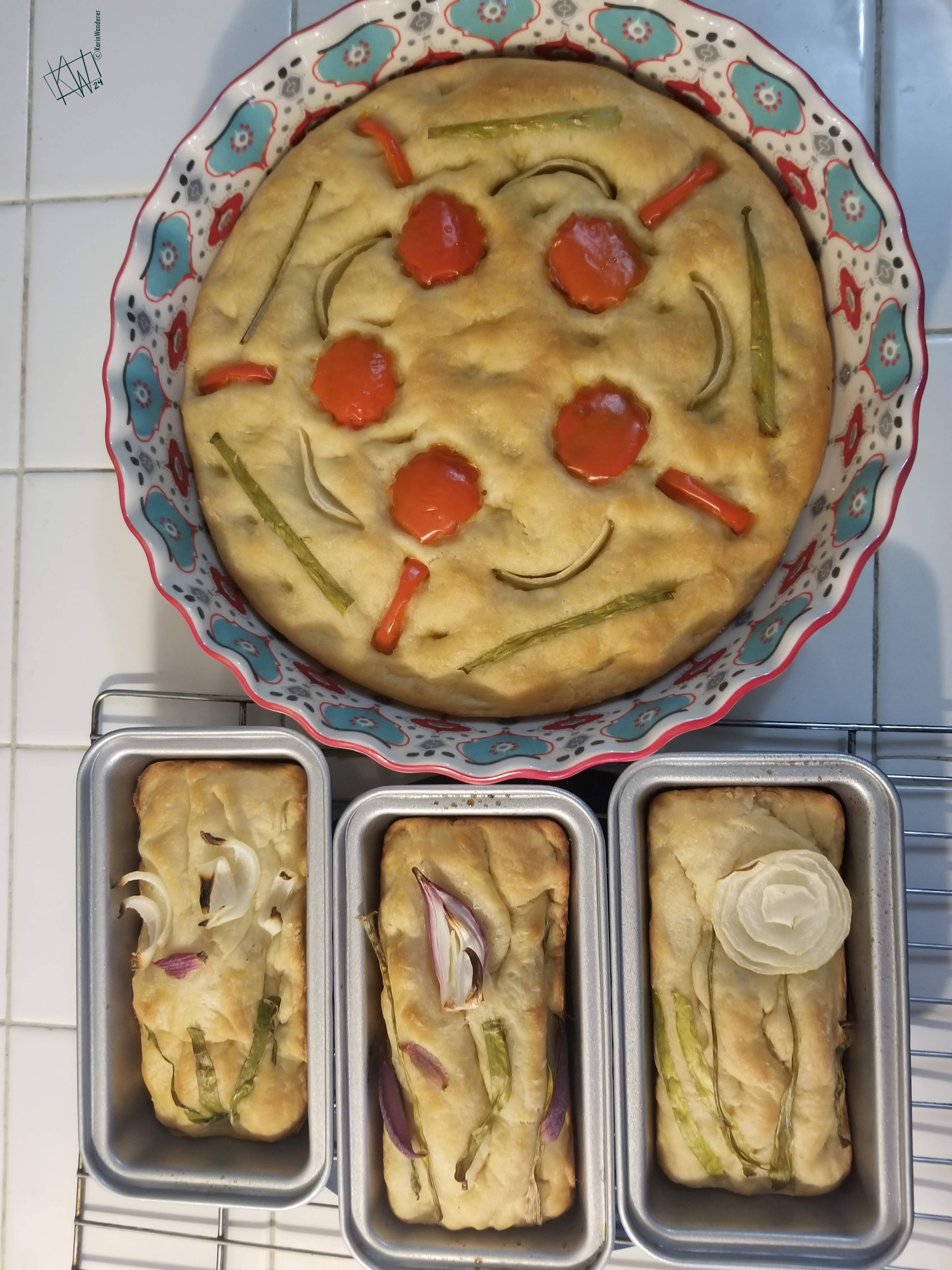 1 round & 4 small loaves of golden brown focaccia, decorated with produce. The round one has a mandala made with red peppers & red & green onions. The rectangular ones have a mess of sliced onions that were supposed to look like flowers.