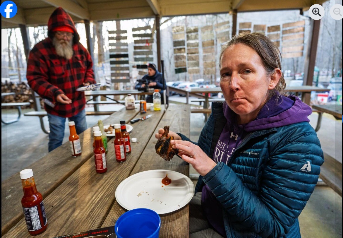A woman is eating fried chicken, laz stands in the background