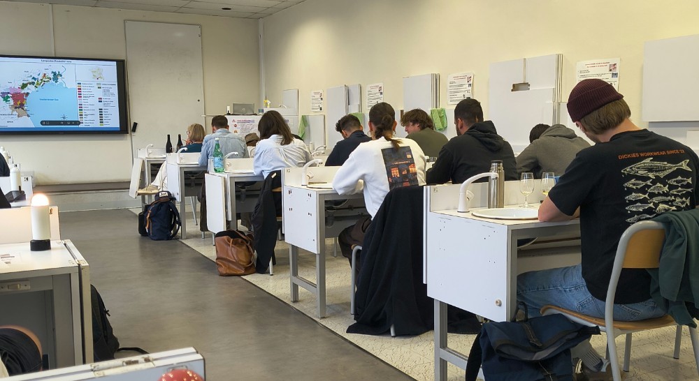 A wine tasting room showing students sitting at their stations examining their wines. At the front a display shows a map of Languedoc wine regions