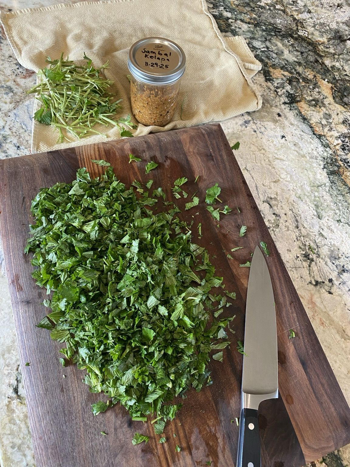We see vibrant green leaves diced on a dark wooden cutting board, a silver knife to the right, and the discarded stems above